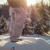 A person wearing gray jogger pants standing on snow with trees and sunset in the background.