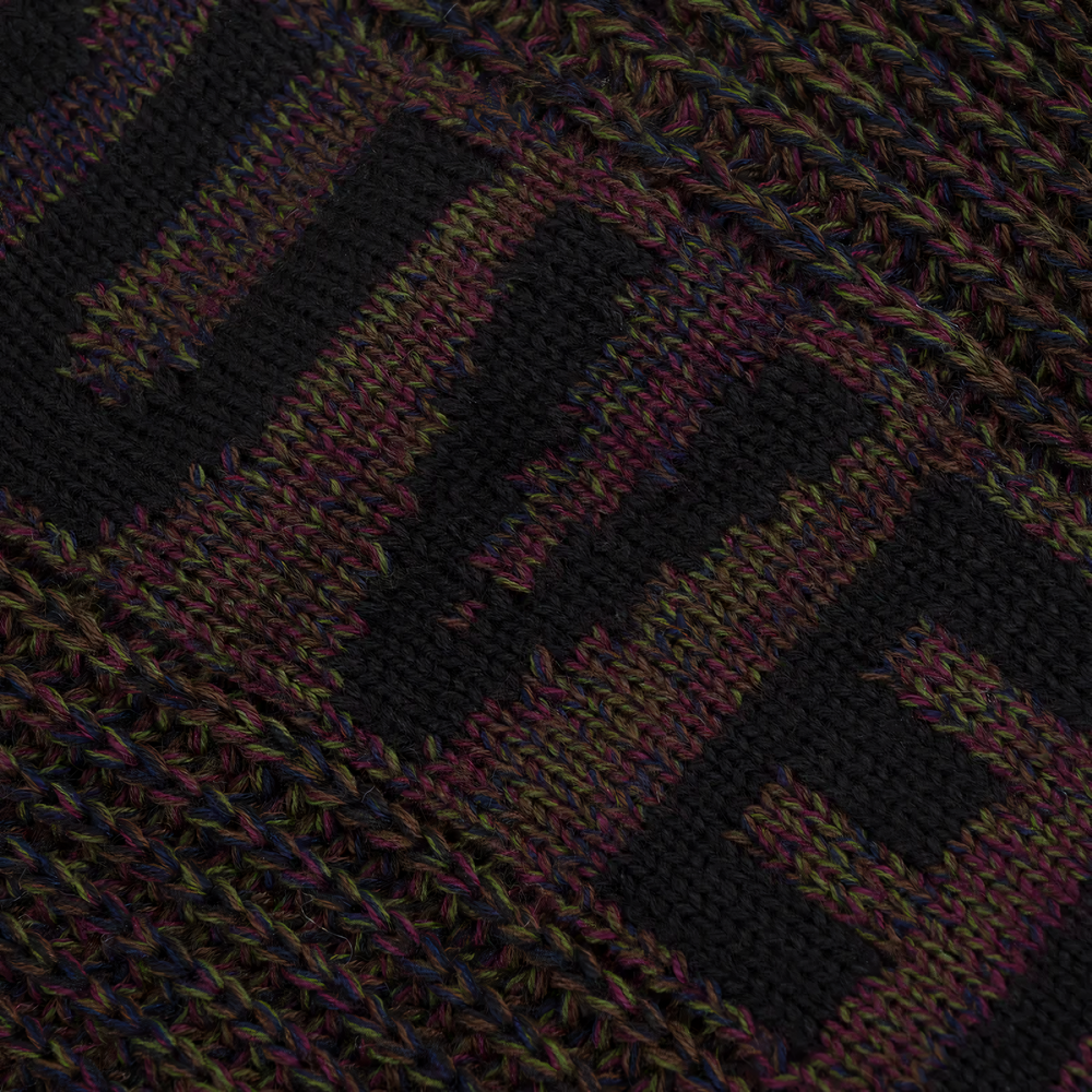 Close-up of a knitted textile with a geometric pattern in black, dark purple, and olive green.