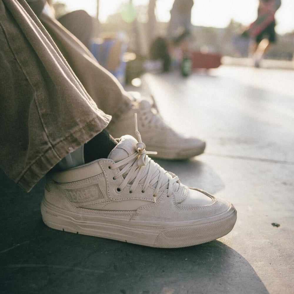 White sneakers worn on a concrete surface with a blurred background of people and trees.
